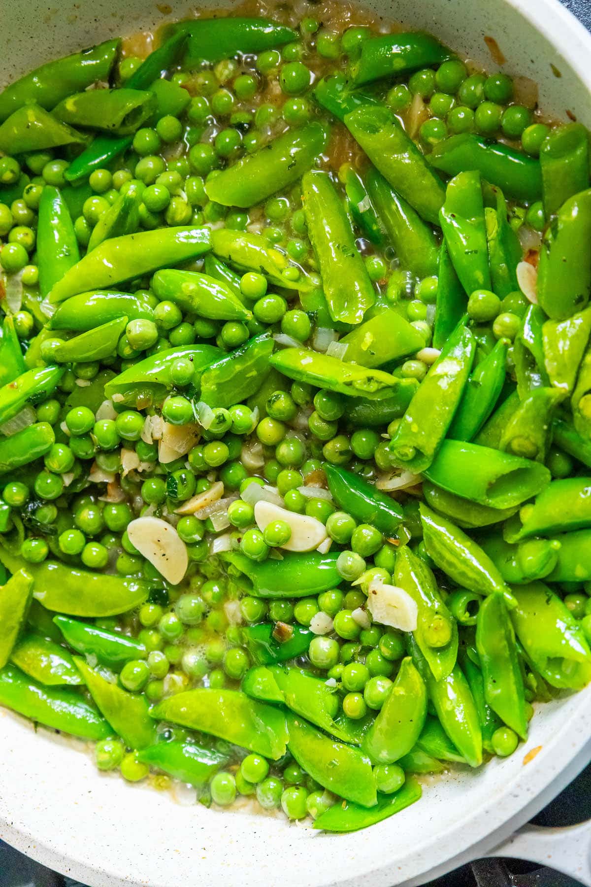 Sautéed peas, snap peas, diced shallot, and mint in a white pan