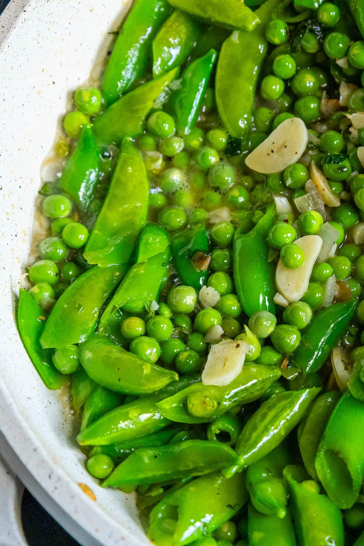 peas sauteeing with garlic white wine sauce in a pan