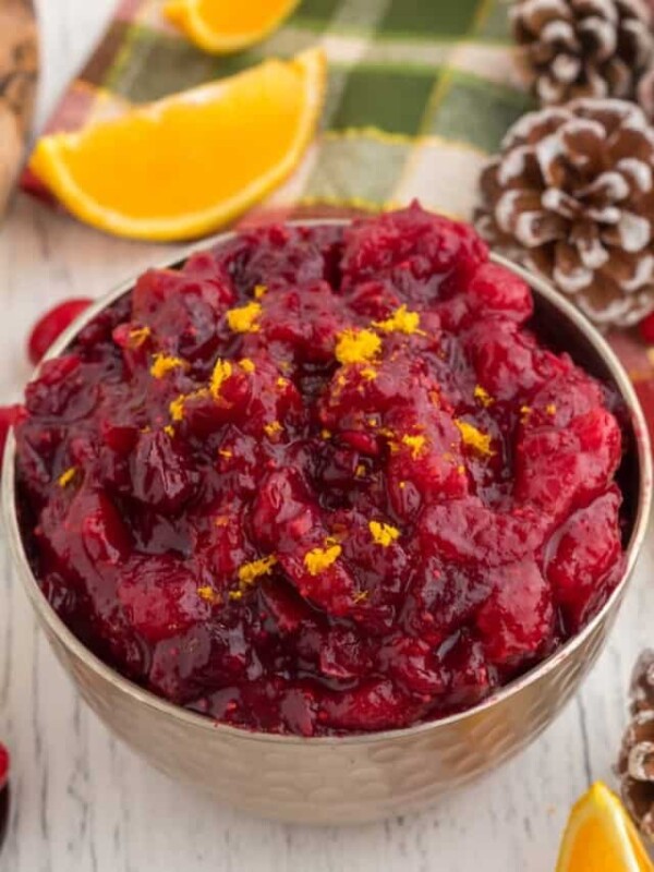 Cranberry sauce in a bowl with oranges and pine cones.