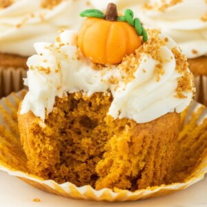 pumpkin cupcake iced with cream cheese frosting and a marzipan pumpkin candy on top