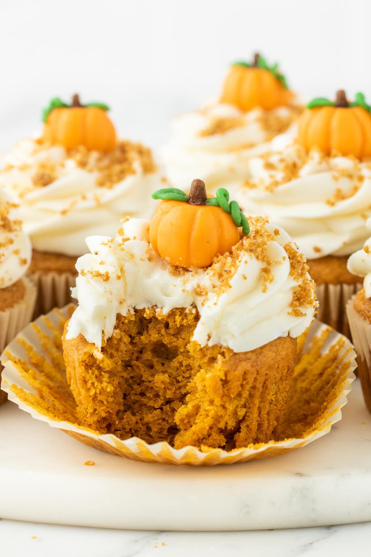baked pumpkin cupcake frosted with cream cheese frosting and topped with a marzipan candy pumpkin