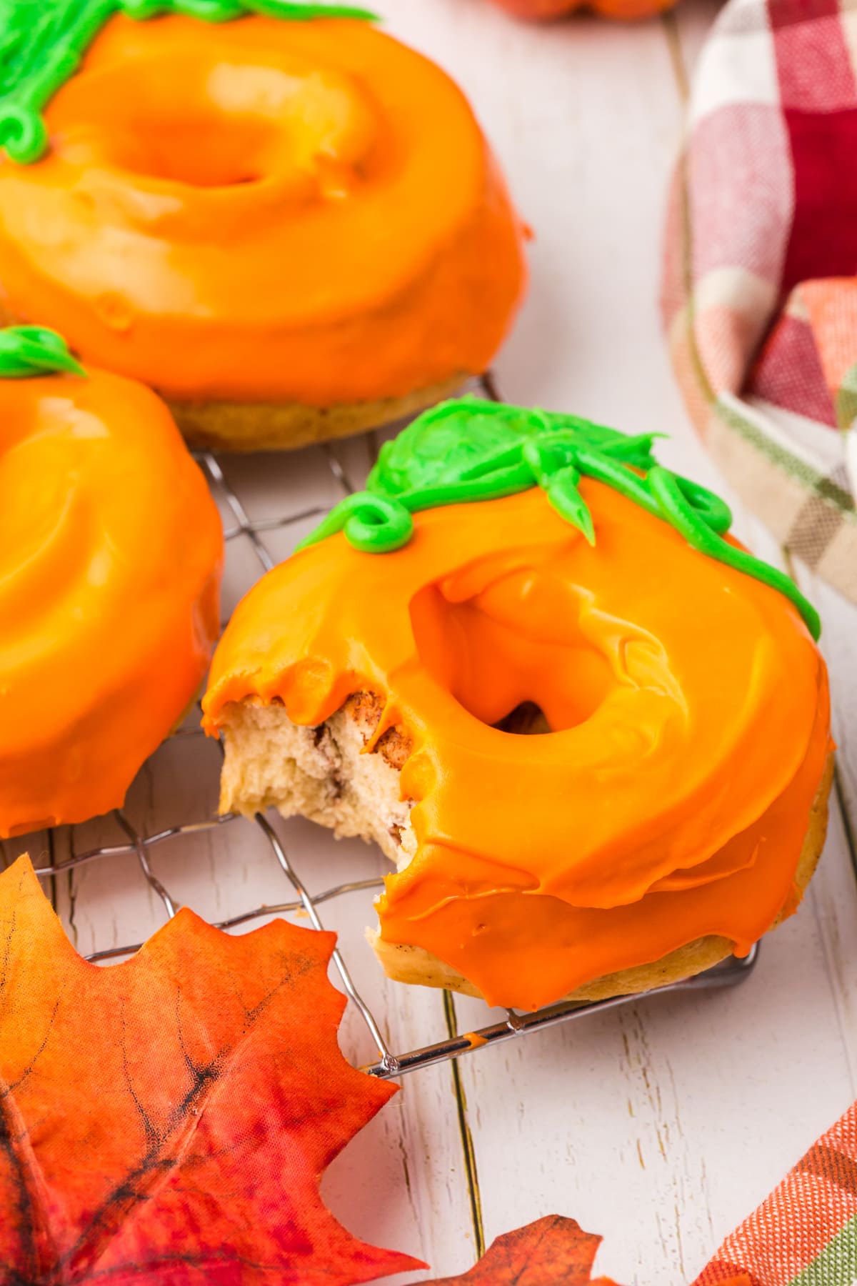 an air fried donut coated in orange and green icing to look like a pumpkin with a bite taken out of it