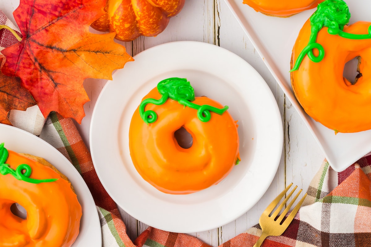 donuts glazed in orange frosting with green leaves and tendrils on top to look like a pumpkin on a plate on a table