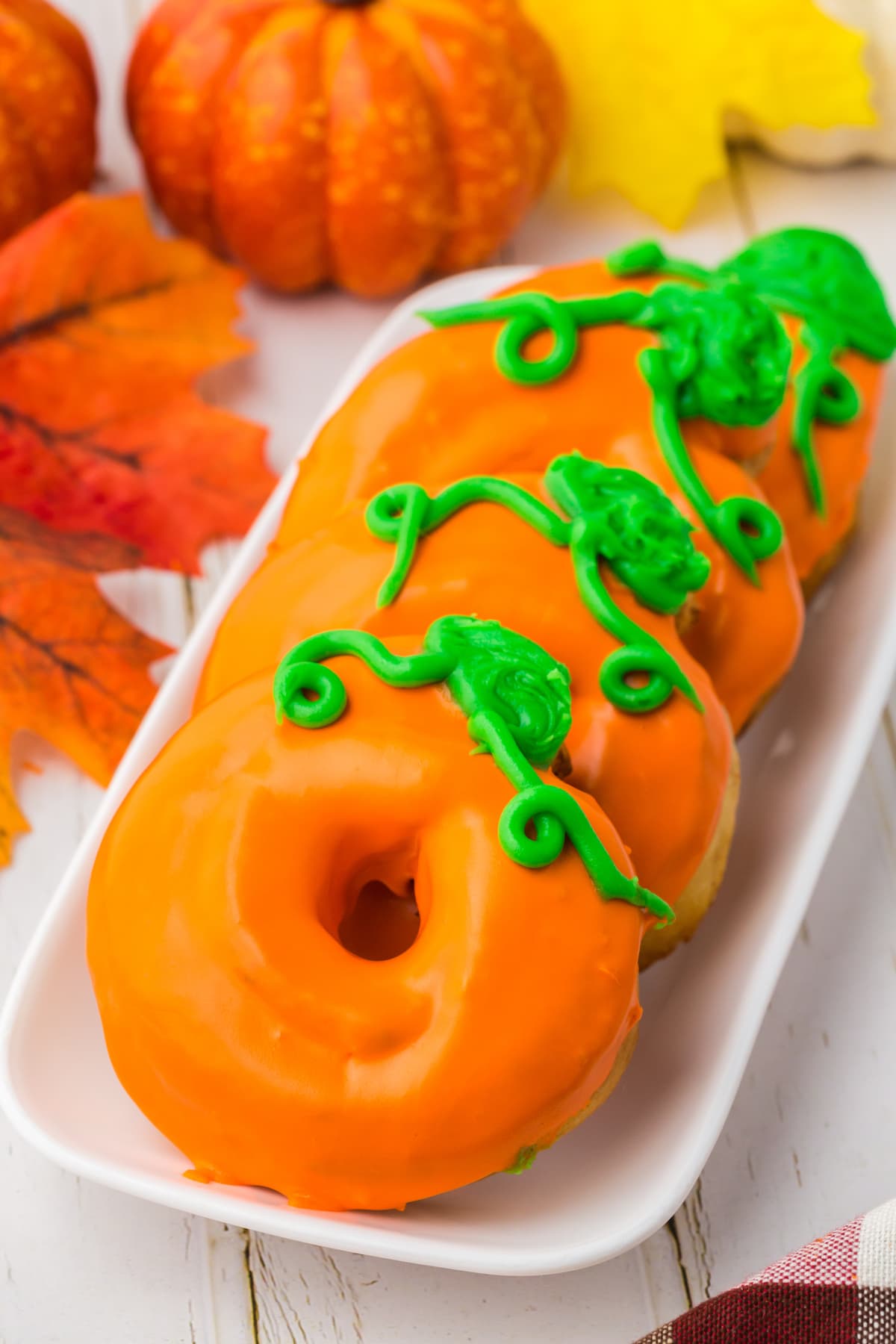 donuts glazed in orange frosting with green leaves and tendrils on top to look like a pumpkin