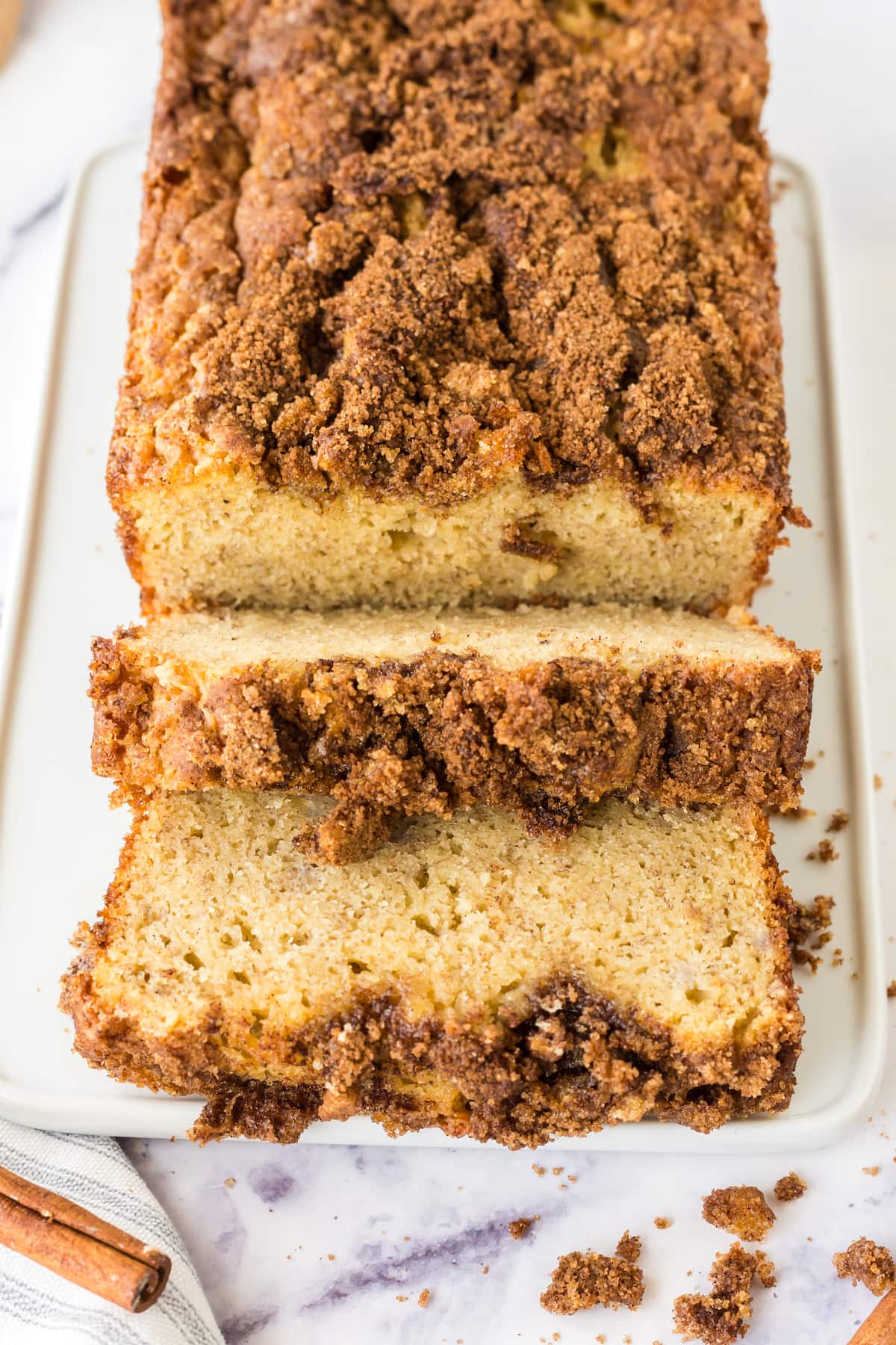 a loaf of banana bread with cinnamon crumble topping sliced on a white plate