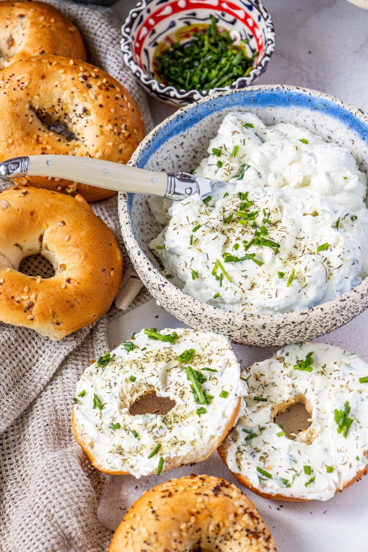 everything bagels on a table covered in dill schmear with chopped chives and pickle seasoning sprinkled on top