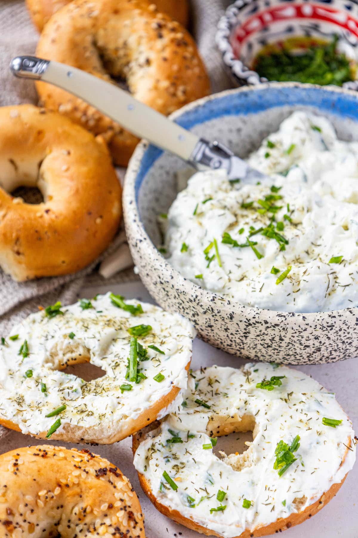 everything bagels on a table covered in dill schmear with chopped chives and pickle seasoning sprinkled on top