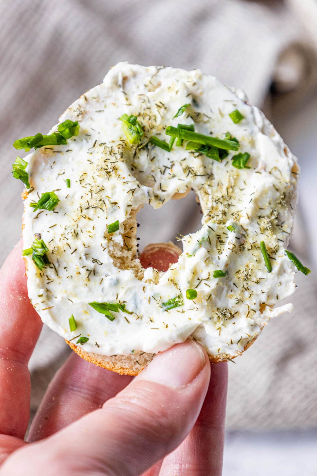 a hand holding an everything bagel with garlic dill schmear all over it