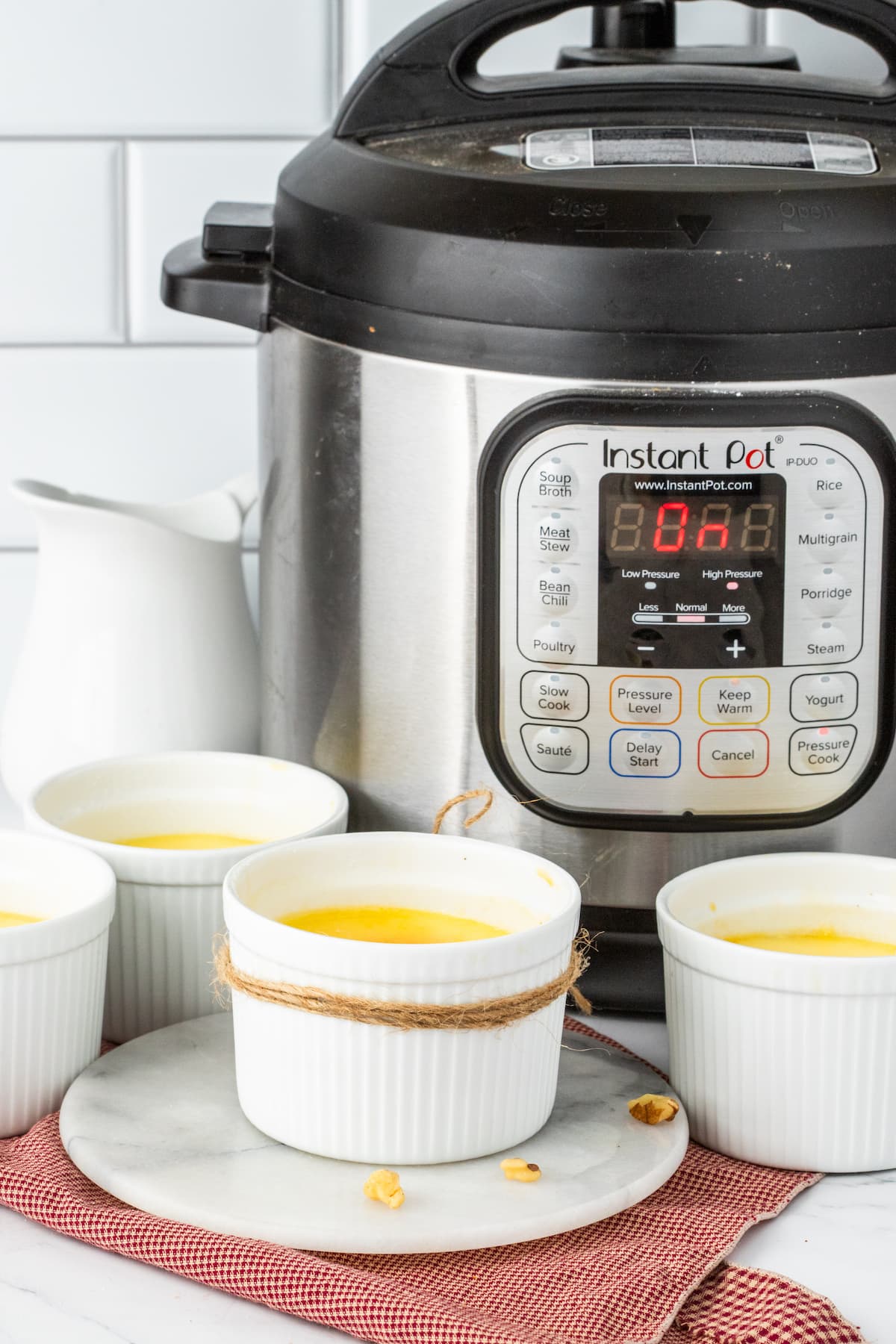 Creme Brûlée in small white ramekins with a twine rope tied around the cups in front of an Instant Pot