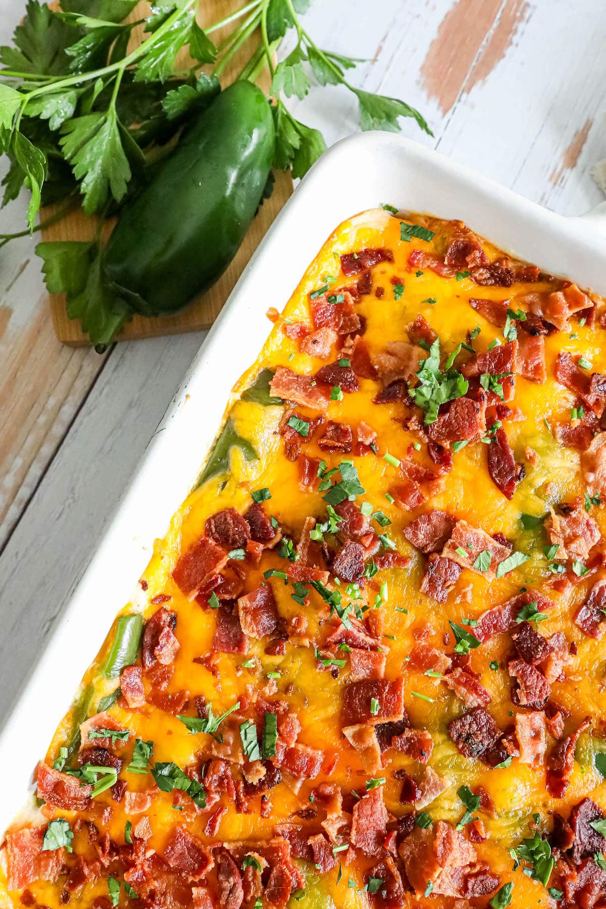 a white casserole dish with chicken jalapeno popper casserole topped with chives, cilantro, cheese, and bacon 