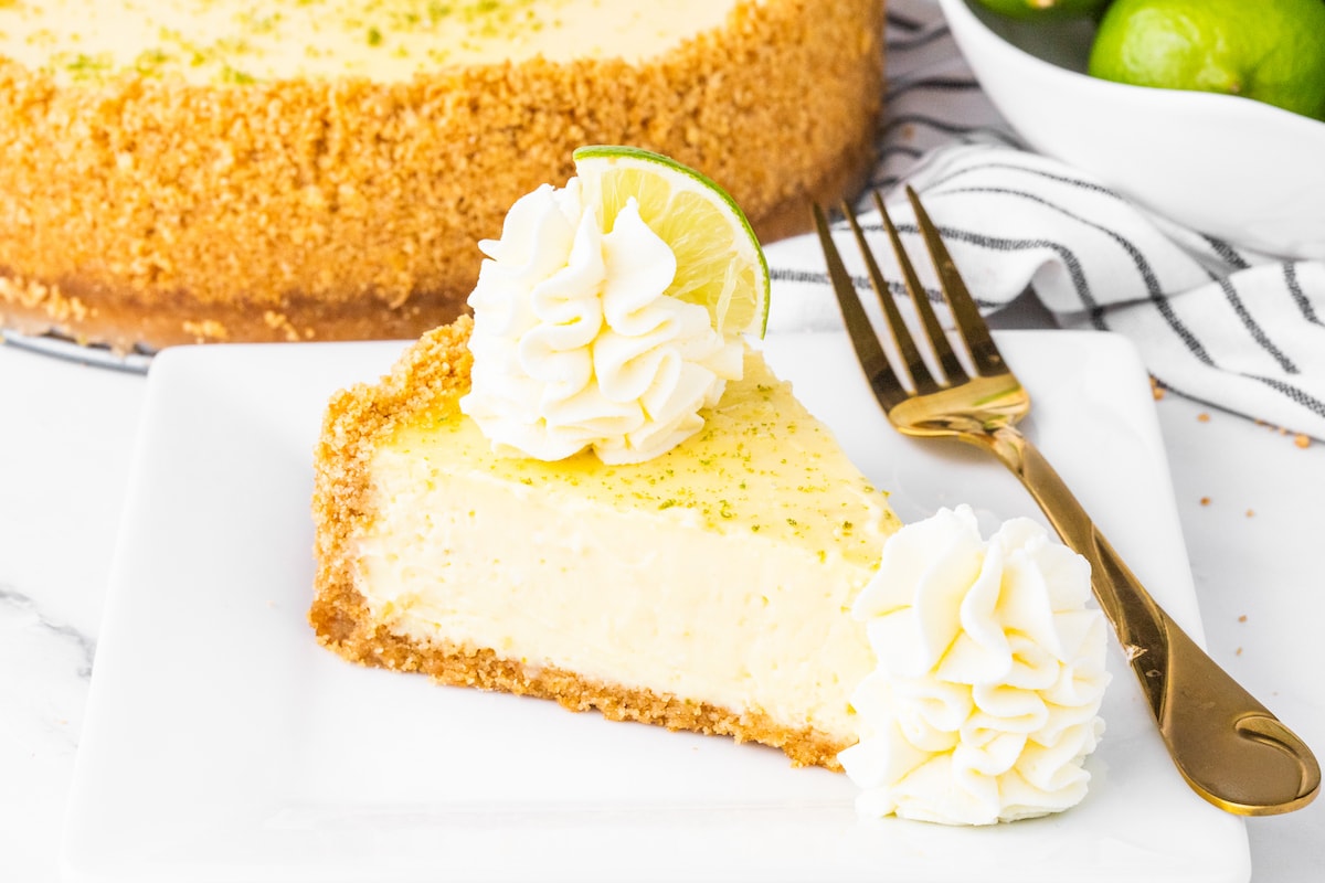 a slice of key lime cheesecake on a plate with a dollop of whipped cream and lime slices on top