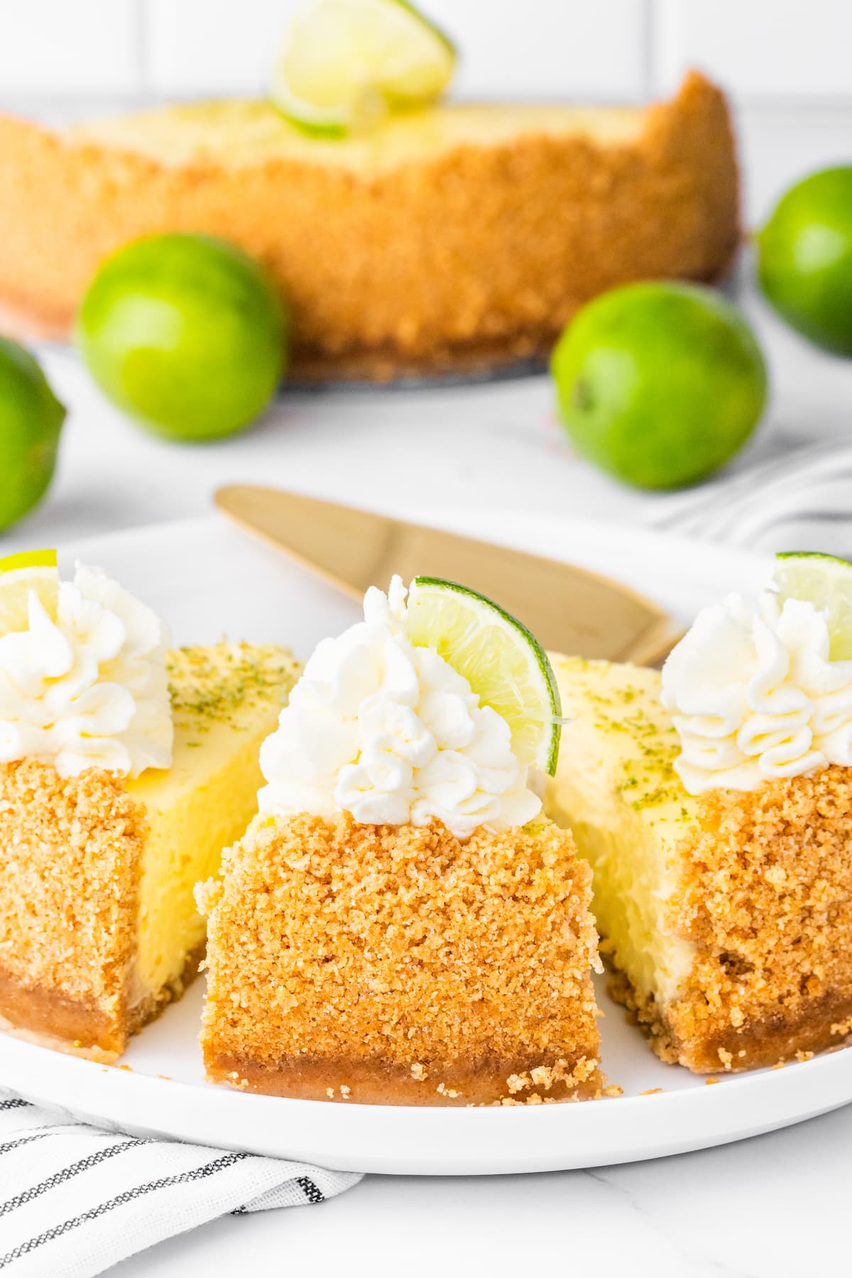 slices of key lime cheesecake on a white plate with whipped cream dollop and a slice of key lime on top