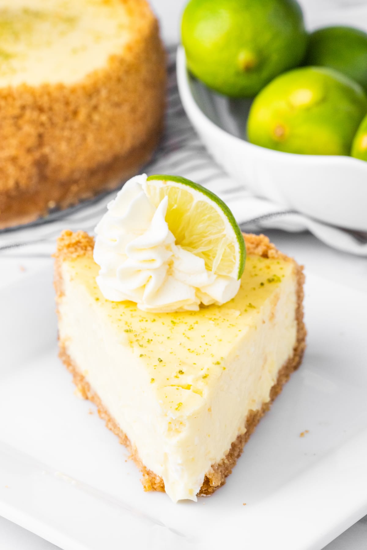 a slice of key lime cheesecake on a plate with a dollop of whipped cream and lime slices on top
