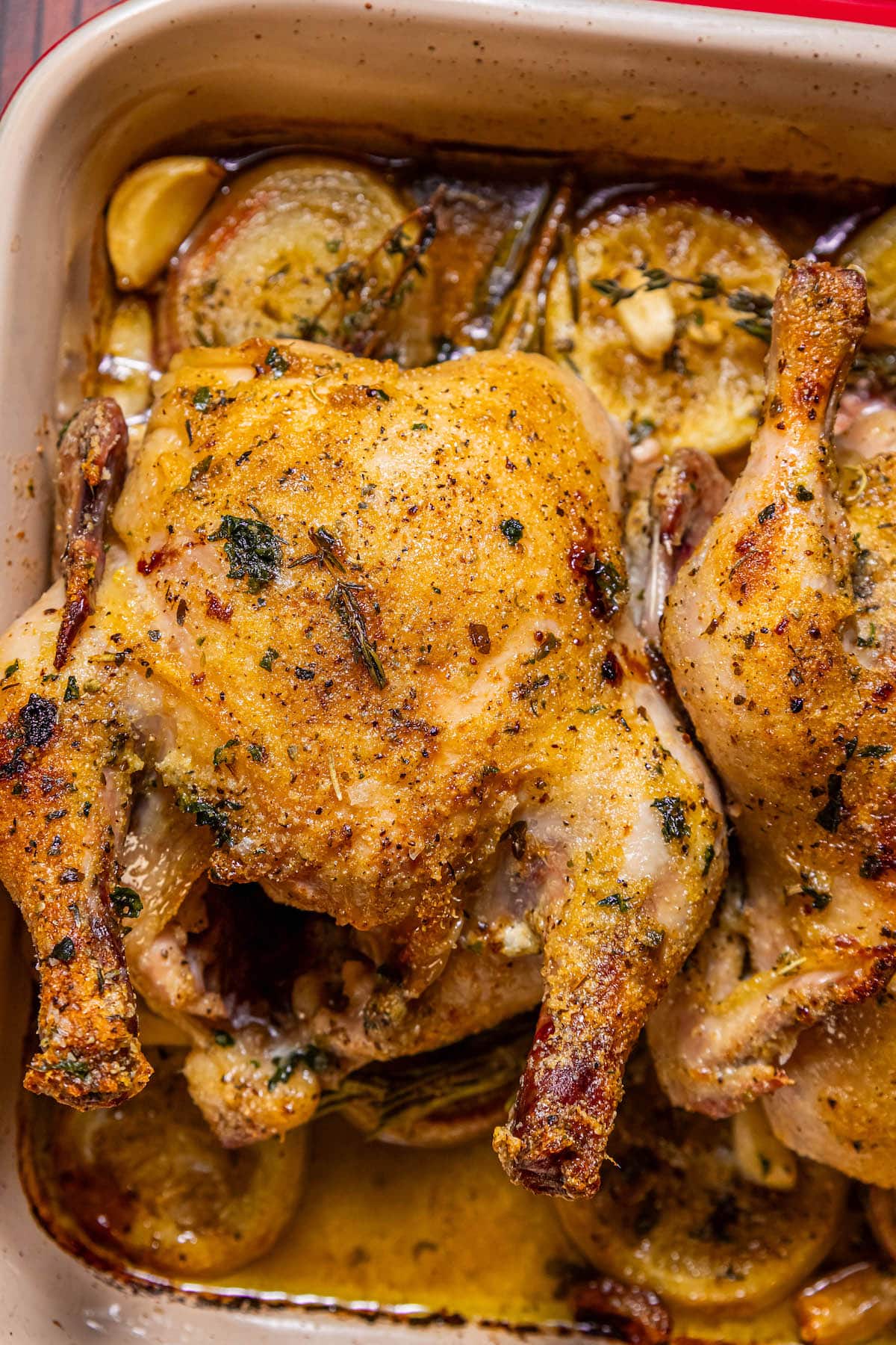 crispy roasted cornish game hen in a square baking dish with lemons, shallots, and garlic