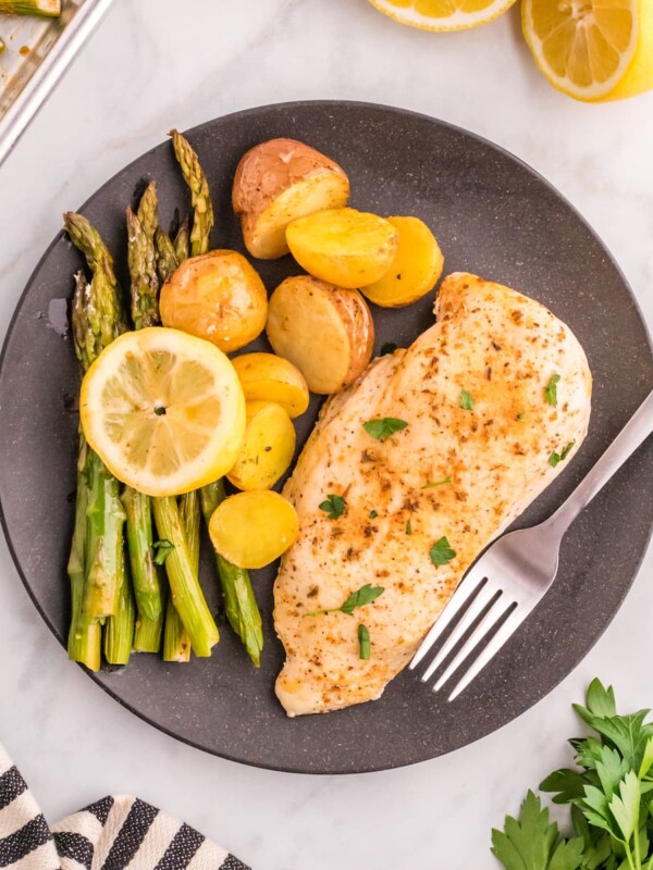 baked chicken breasts, lemon slices potatoes, and asparagus on a baking sheet