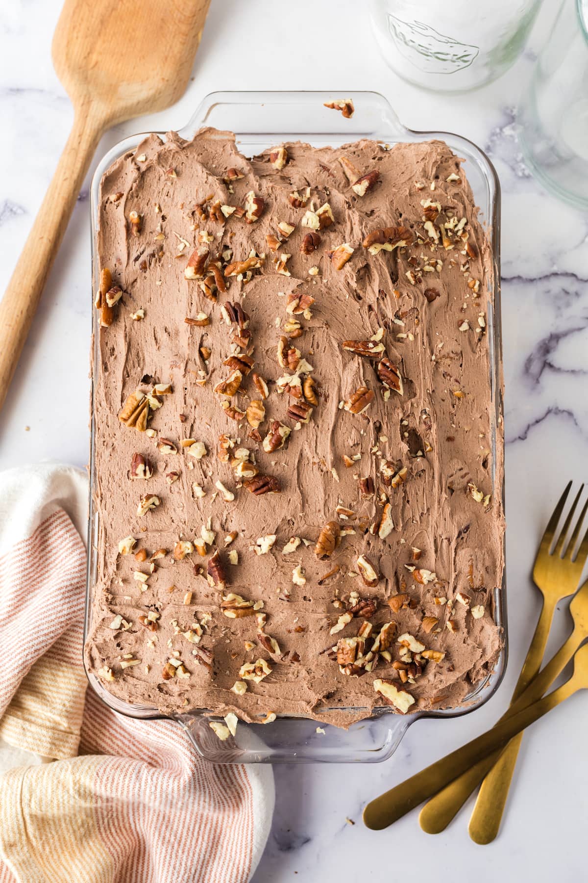chocolate cake with chocolate icing topped with nuts in a casserole dish on a table