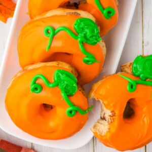 air fried pumpkin donuts with orange frosting and green pumpkin stem icing on top on a plate