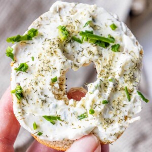 a hand holding an everything bagel with garlic dill schmear all over it