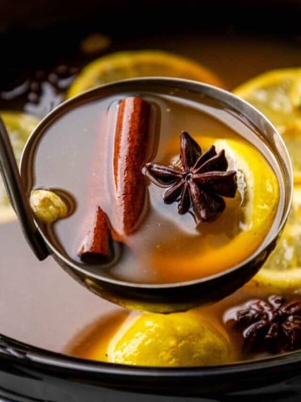 A spoon full of mulled wine with cinnamon sticks and lemons.