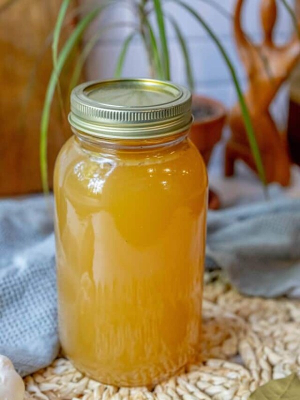 A jar of honey on a table next to a plant.