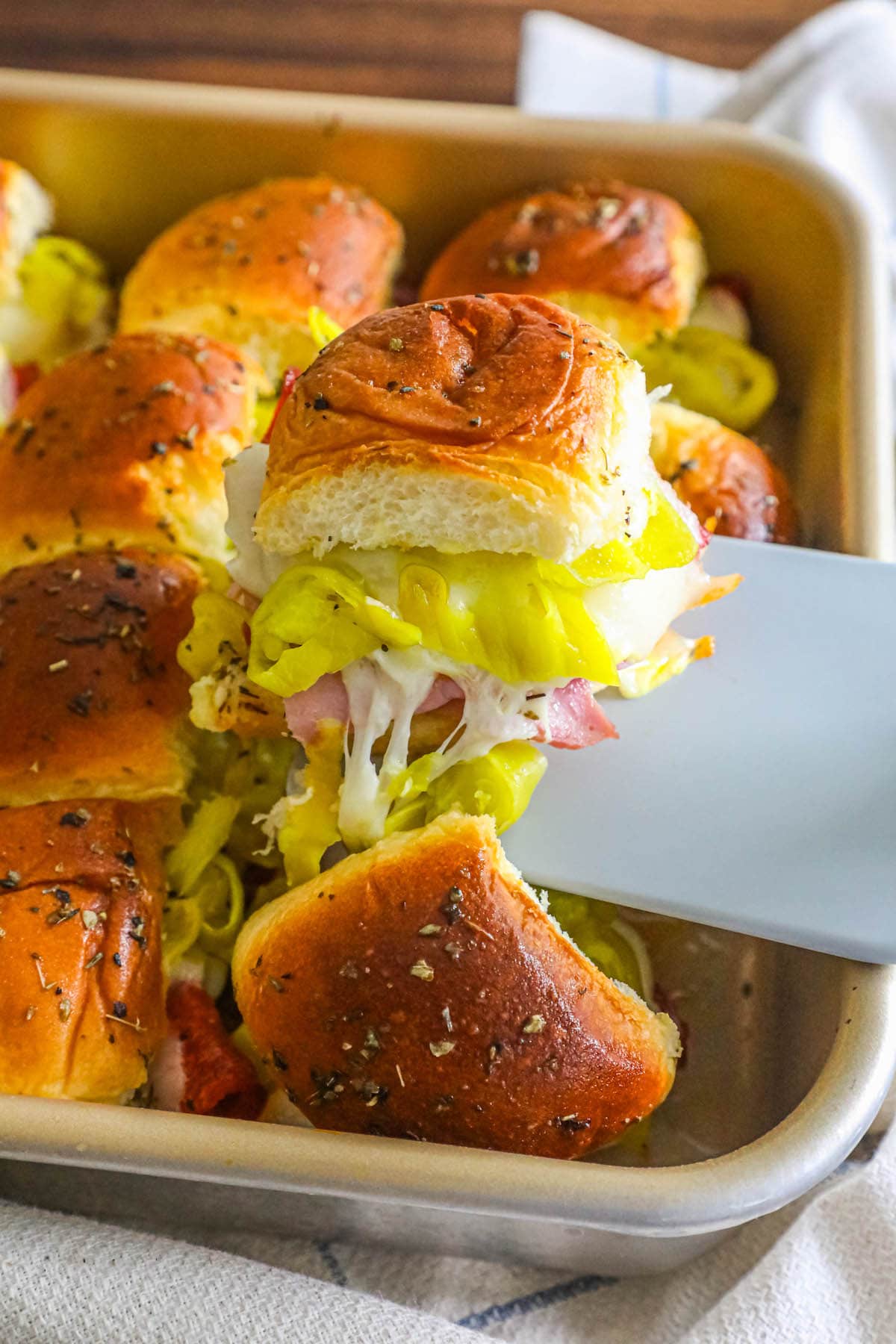 rolls with ham, cheese, and pepperoncini in between them, one being lifted out