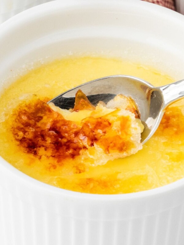 a spoon scooping burnt sugar topping of a creme brûlée in a white ramekin