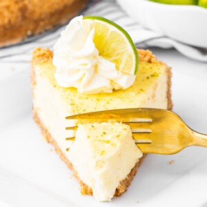 a fork cutting into a slice of key lime cheesecake with a dollop of whipped cream and a slice of key lime on top