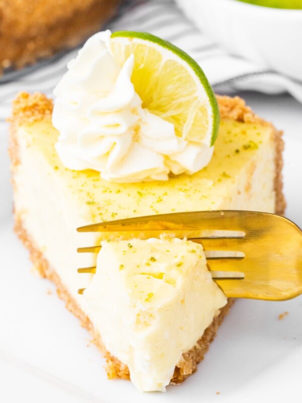 a fork cutting into a slice of key lime cheesecake with a dollop of whipped cream and a slice of key lime on top