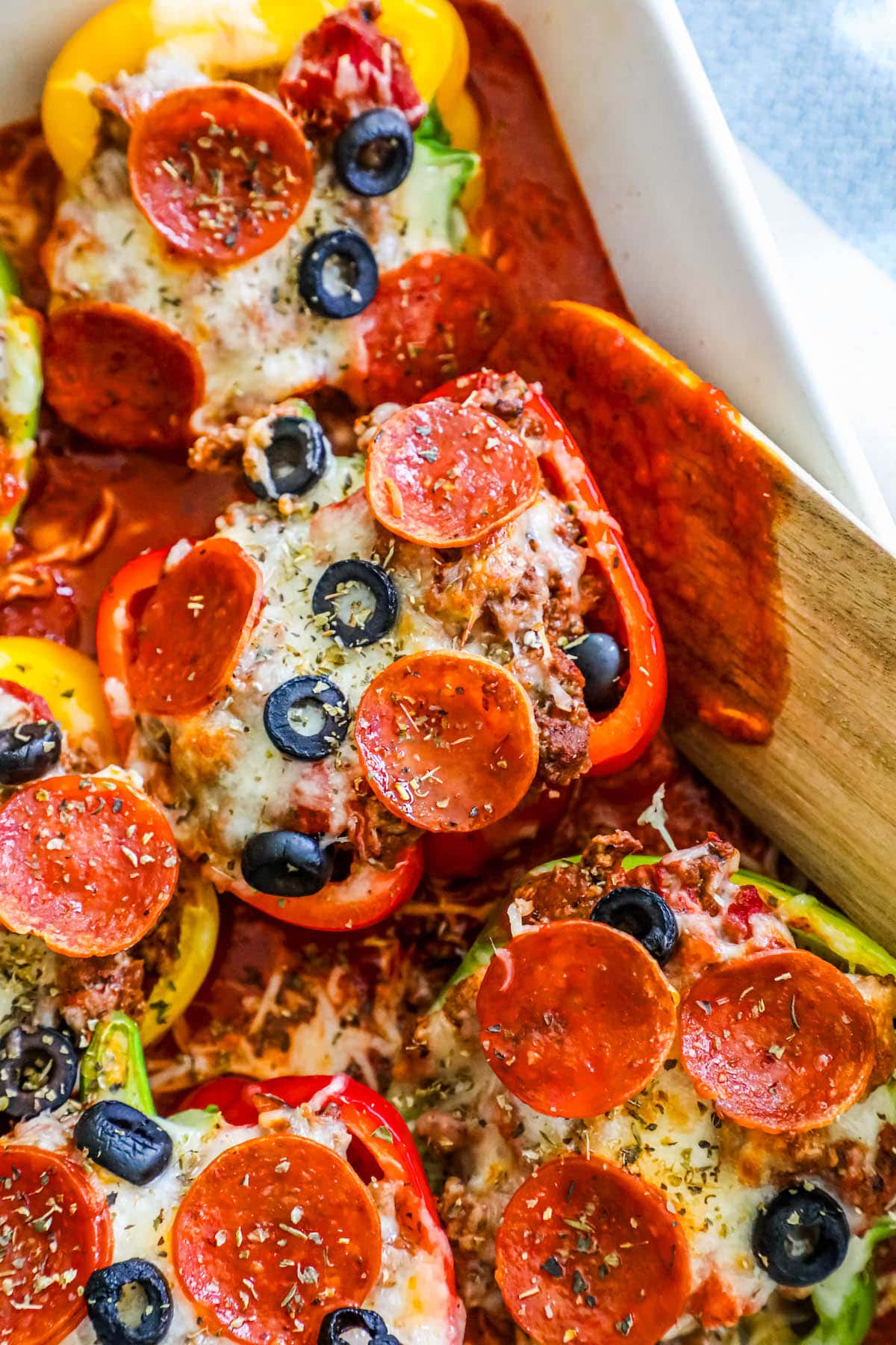 bell peppers filled with pizza toppings over marinara sauce in a white pan