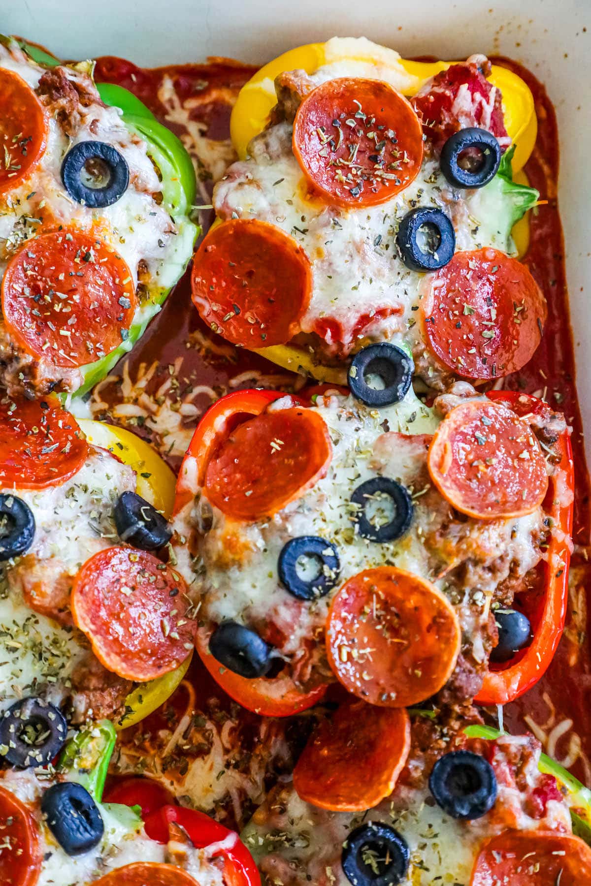 bell peppers filled with pizza toppings over marinara sauce in a white pan