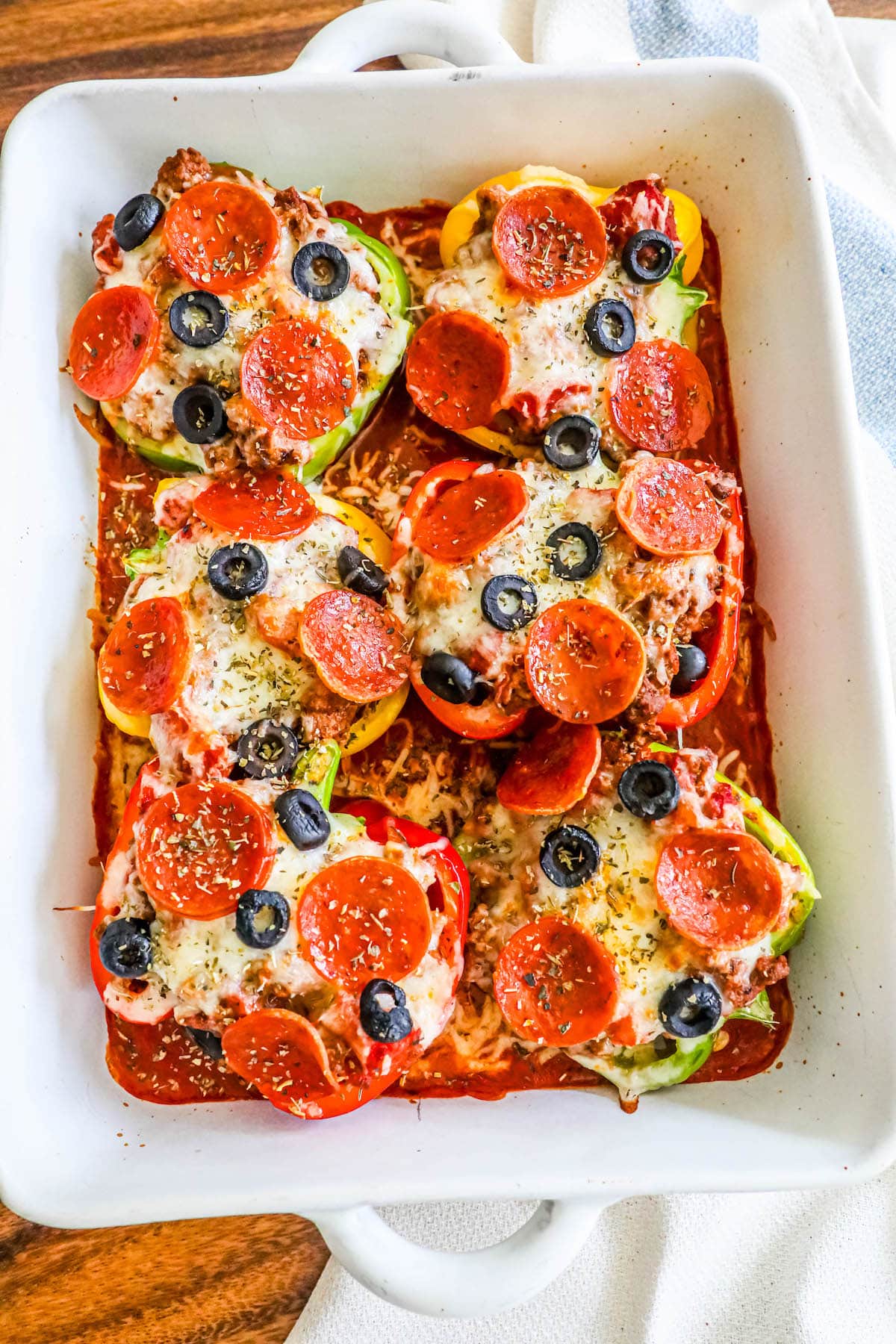 bell peppers filled with pizza toppings over marinara sauce in a white pan