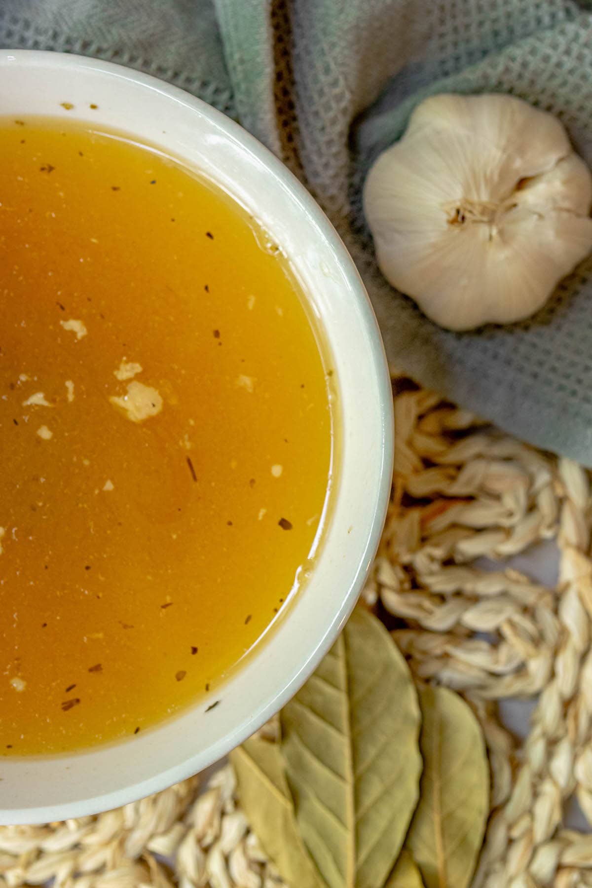 bowl of yellow stock with bat leaves and garlic in the background