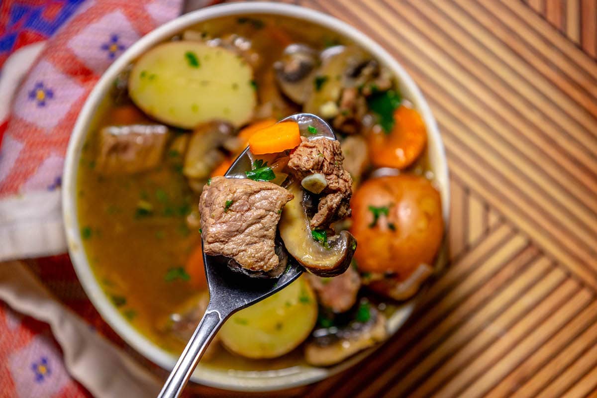 stew meat, carrots, potatoes, and minced parsley in a bowl, some on a spoon