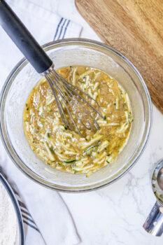 zucchini shreds mixed into bread batter in a glass bowl