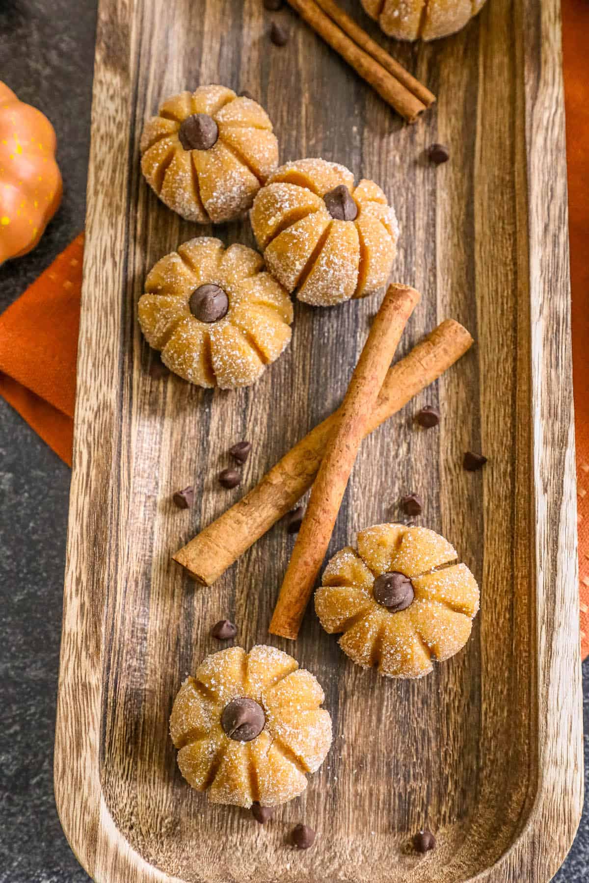 Pumpkin cookies with cinnamon sticks on a wooden tray.