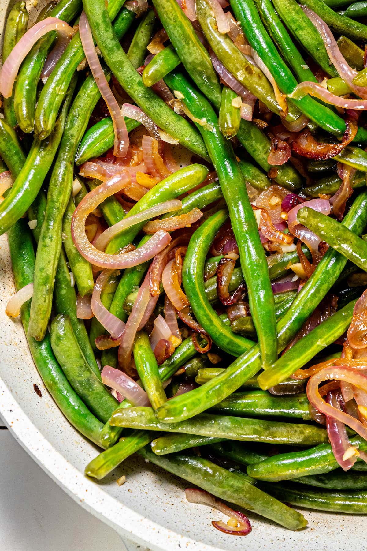 Sautéed green beans and red onion in a skillet.
