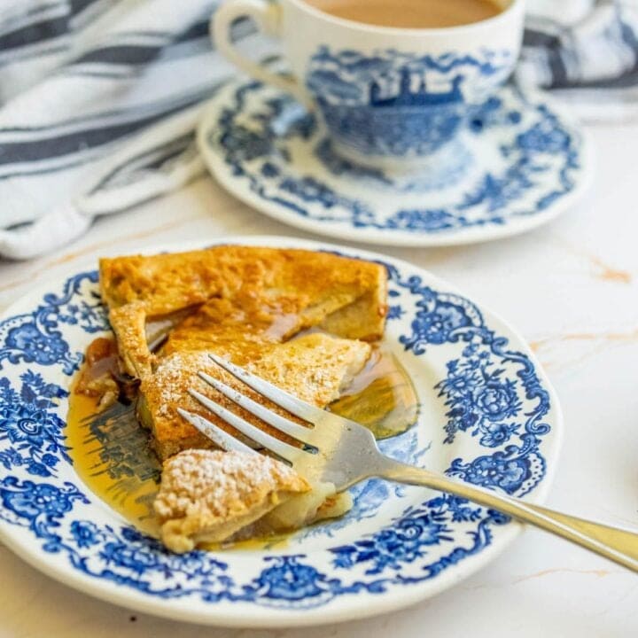A slice of apple pie on a blue and white plate next to a cup of coffee, reminiscent of a cinnamon apple pancake.