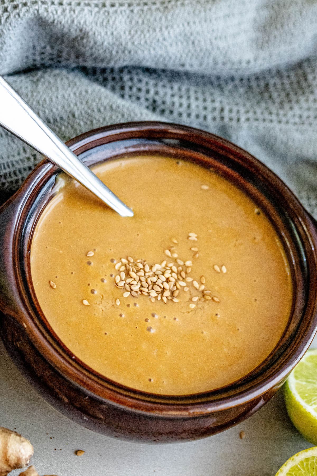 creamy dressing with sesame seeds with limes and ginger around it, spoon in it