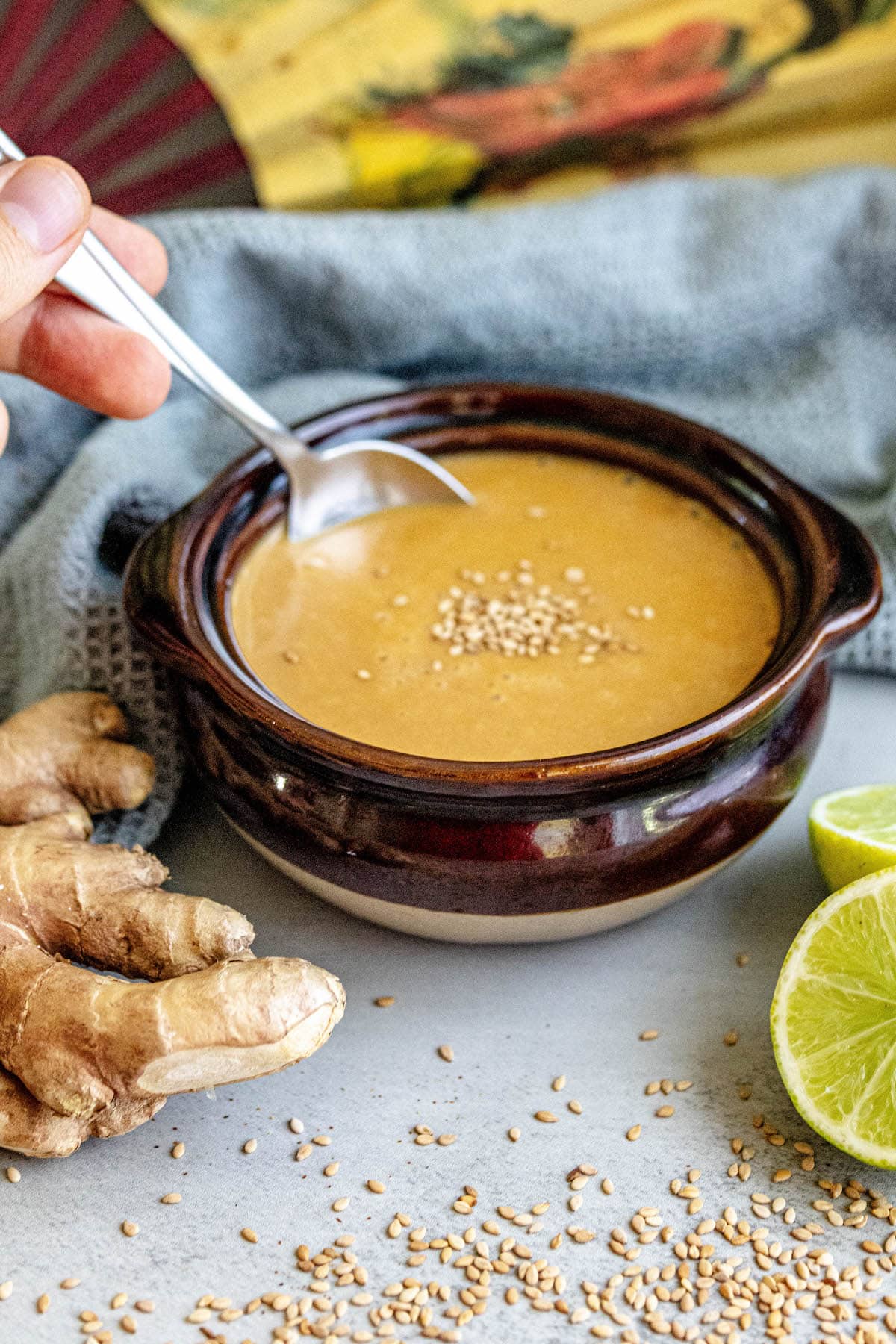 spoon dipping into creamy dressing with sesame seeds with limes and ginger around it