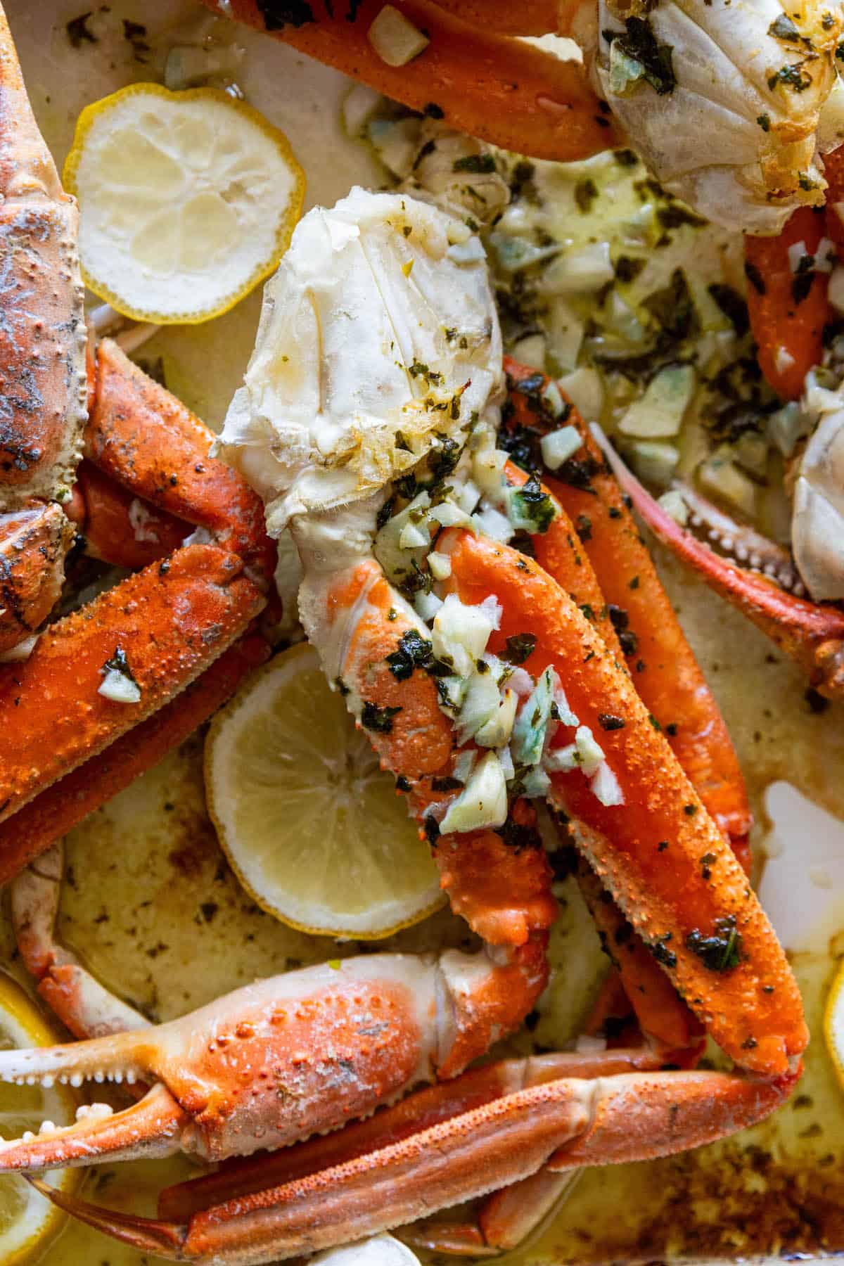 Baked snow crab legs with lemon and herbs on a baking sheet.