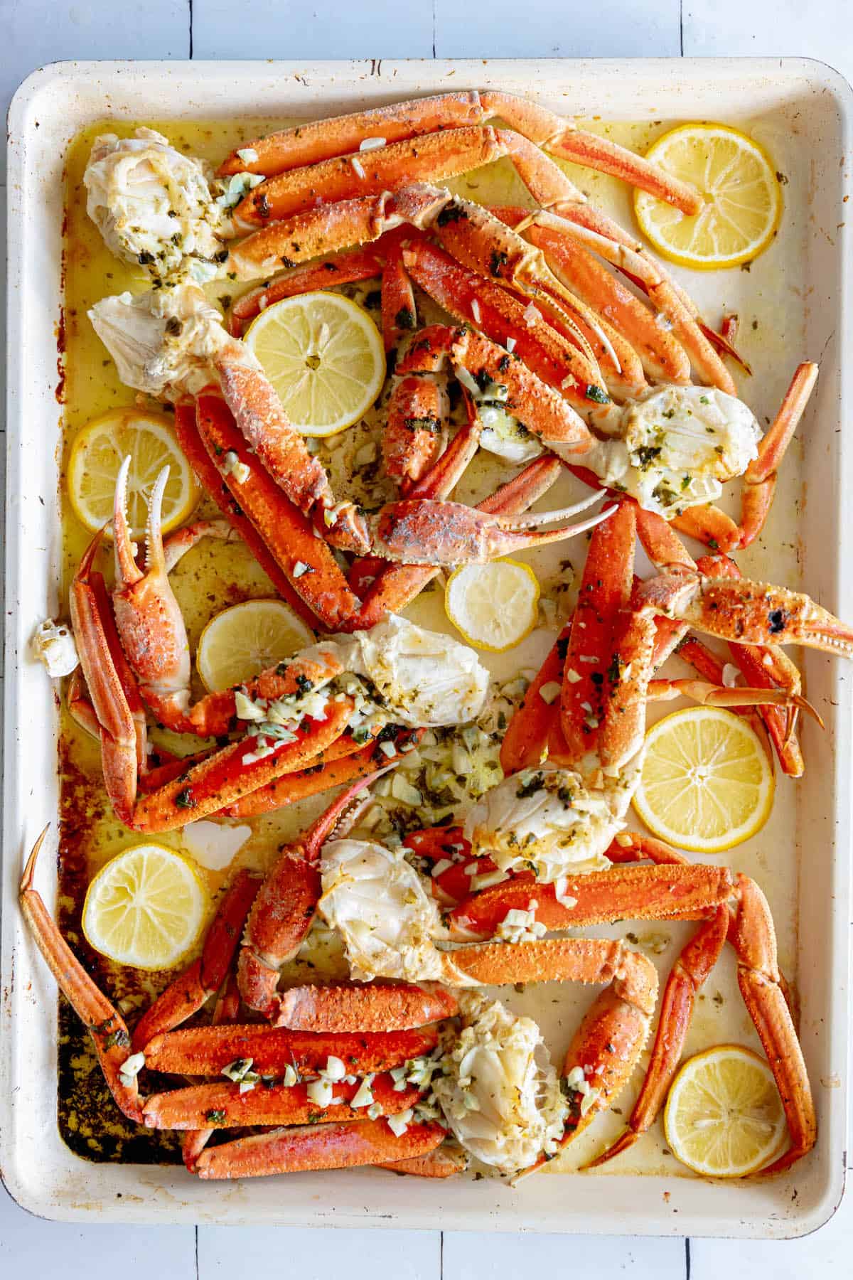 A baking sheet with baked snow crab legs and lemon wedges on it.