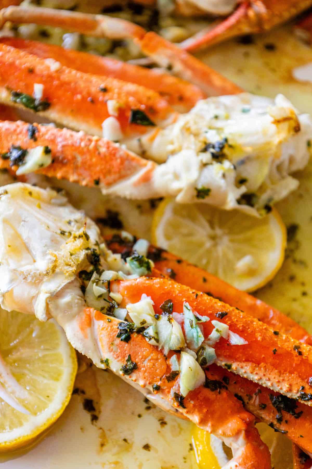 Baked snow crab legs on a plate with lemon wedges.