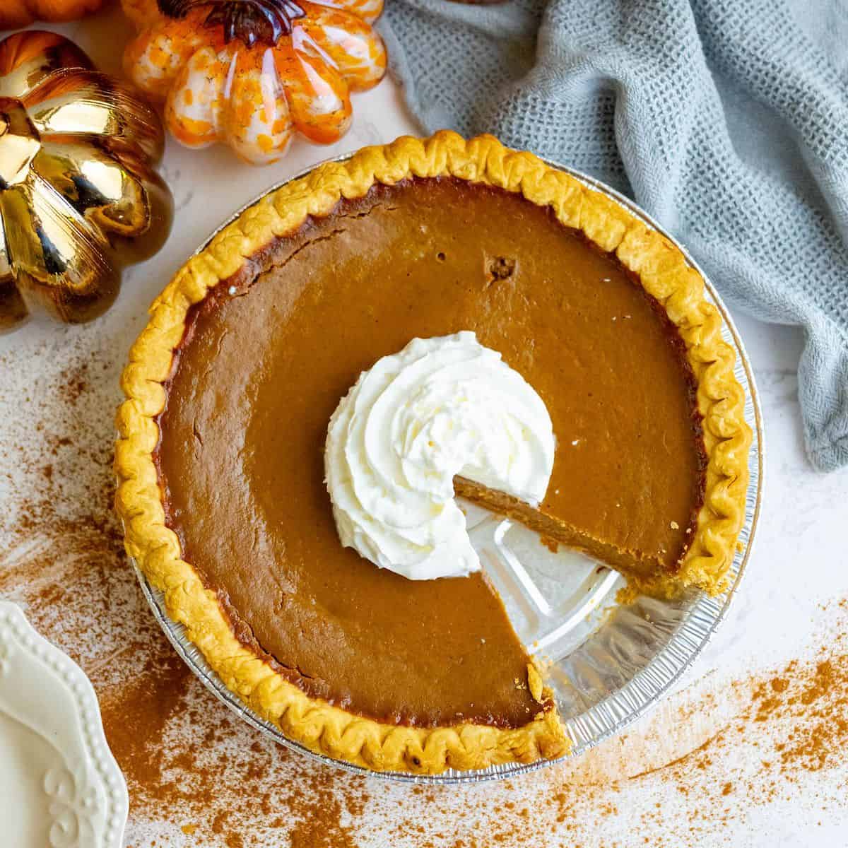 A spicy pumpkin pie with whipped cream and a slice taken out.