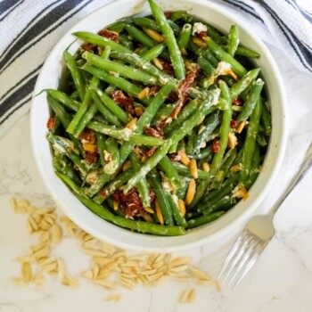 Cheesy green beans baked with sun-dried tomatoes in a white bowl.