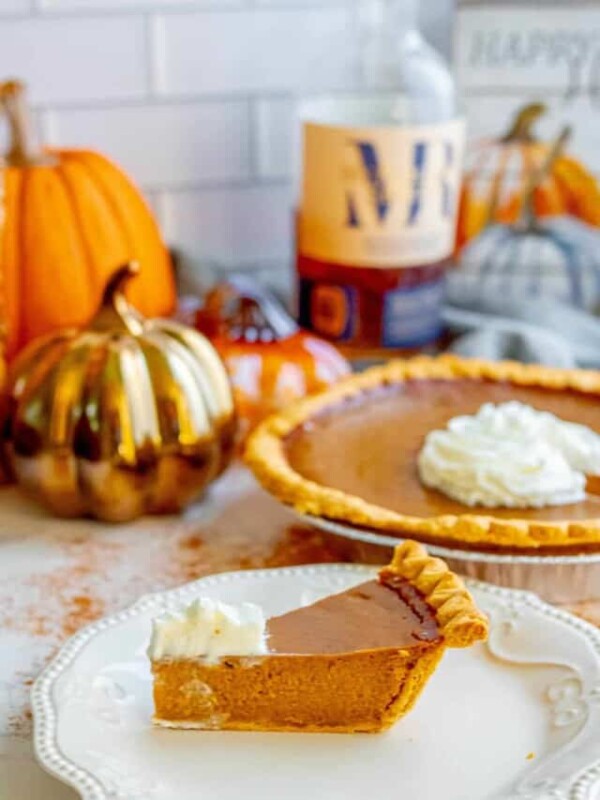 A slice of pumpkin pie on a plate next to a bottle of bourbon.