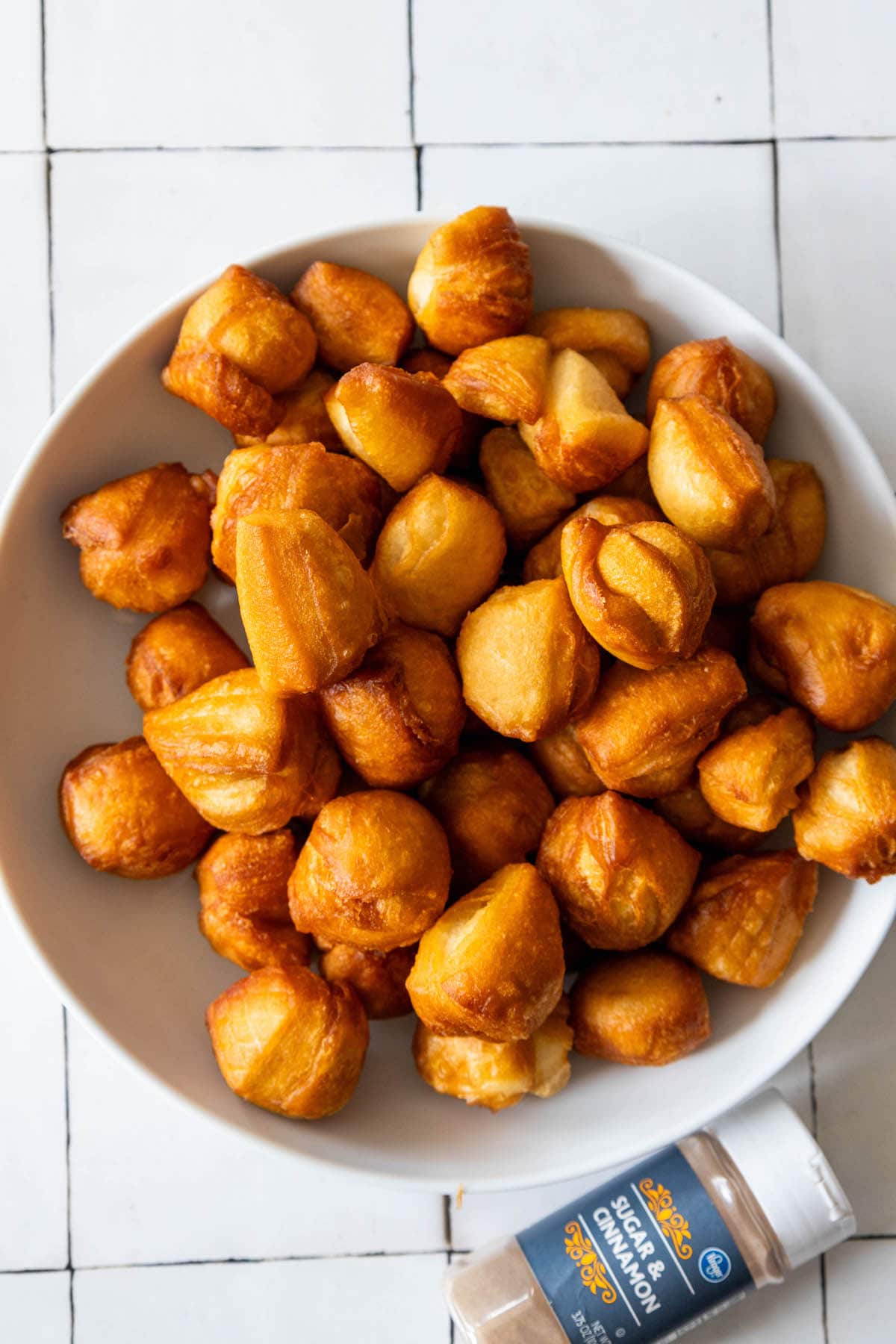 A bowl of fried cinnamon biscuits on a tiled floor.