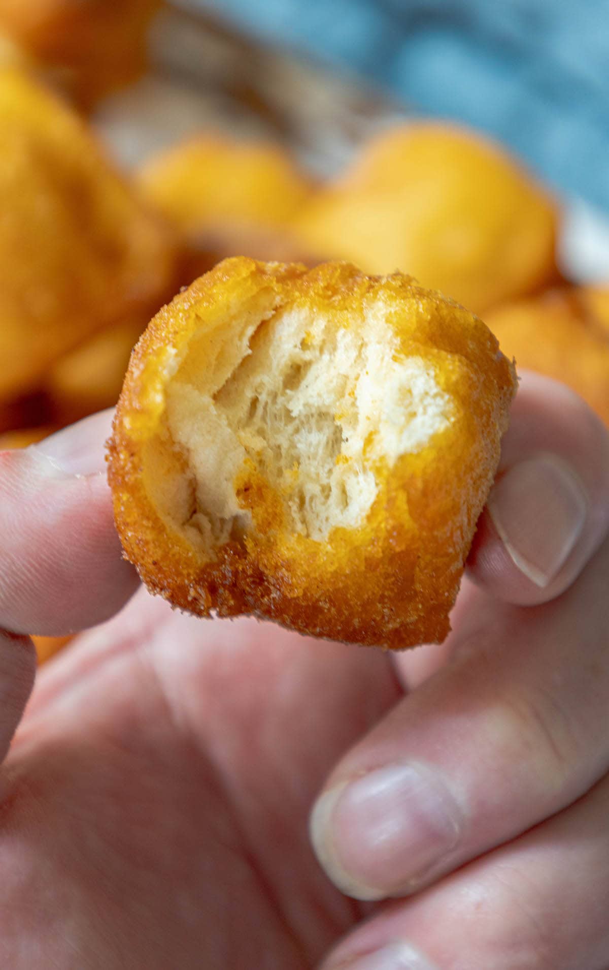 A person's hand holding a bite of a fried doughnut.