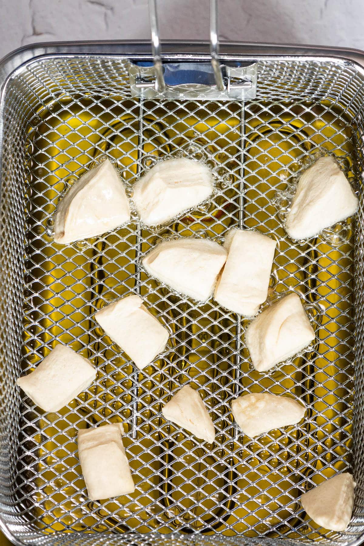 A wire mesh basket filled with pieces of fried bread.