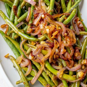 Sautéed green beans and red onion on a white plate.