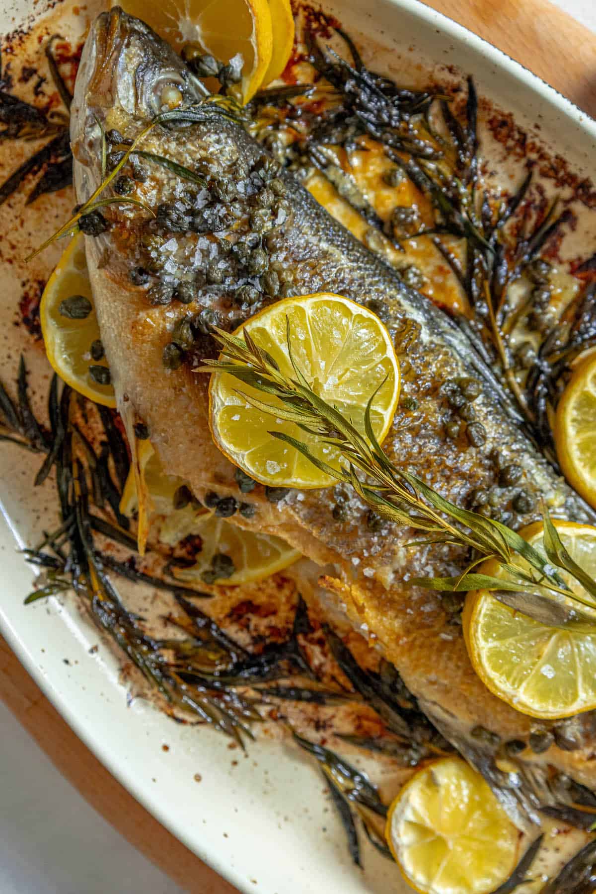 A roasted Branzino fish with lemon slices on a plate.